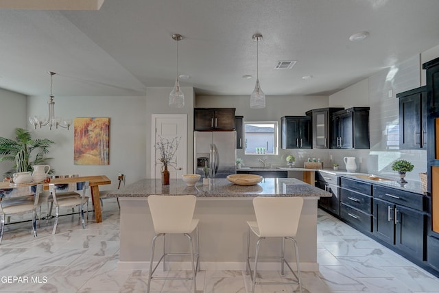 kitchen featuring a kitchen island, visible vents, stainless steel fridge with ice dispenser, hanging light fixtures, and light stone countertops