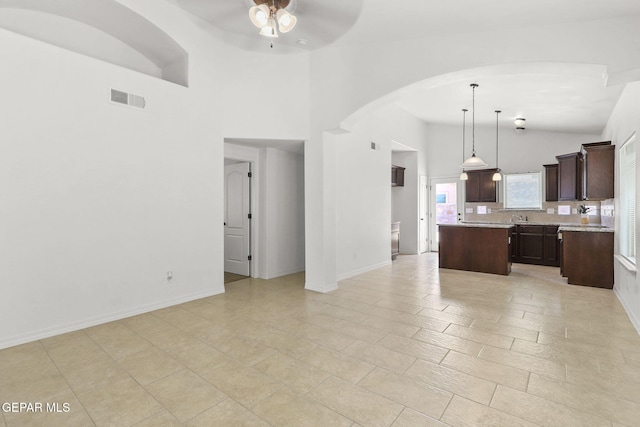 kitchen with dark brown cabinetry, ceiling fan, decorative light fixtures, high vaulted ceiling, and a kitchen island