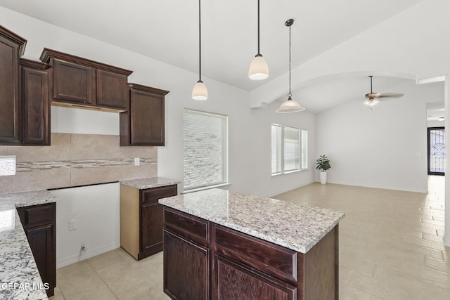 kitchen featuring ceiling fan, a center island, hanging light fixtures, light stone counters, and vaulted ceiling