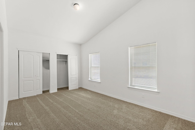 unfurnished bedroom featuring carpet flooring, high vaulted ceiling, and multiple closets