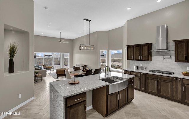 kitchen featuring tasteful backsplash, wall chimney range hood, light parquet floors, sink, and light stone countertops