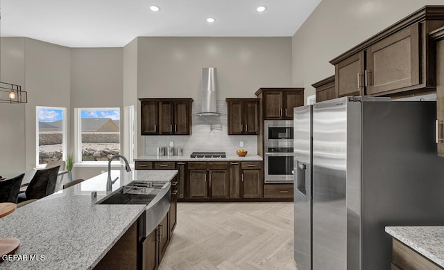 kitchen with light parquet floors, tasteful backsplash, wall chimney exhaust hood, appliances with stainless steel finishes, and sink