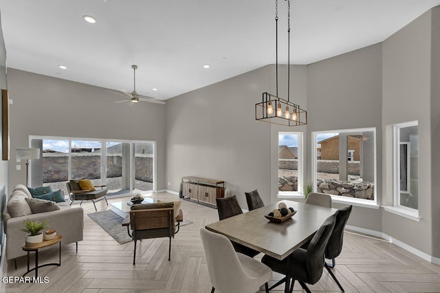 dining space featuring light parquet floors, ceiling fan with notable chandelier, a wealth of natural light, and a towering ceiling