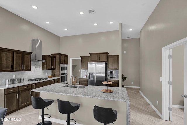 kitchen featuring backsplash, appliances with stainless steel finishes, sink, wall chimney range hood, and light parquet flooring