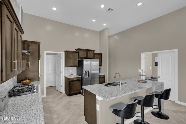 kitchen featuring a high ceiling, light stone countertops, a kitchen bar, sink, and light parquet floors