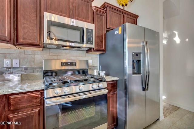 kitchen with tasteful backsplash, light stone countertops, appliances with stainless steel finishes, and light tile floors