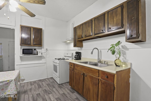 kitchen with ceiling fan, white gas range oven, dark wood-type flooring, dark brown cabinetry, and stainless steel microwave