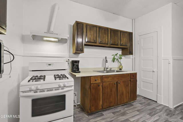 kitchen featuring sink, white gas range, dark brown cabinets, dark wood-type flooring, and wall chimney range hood