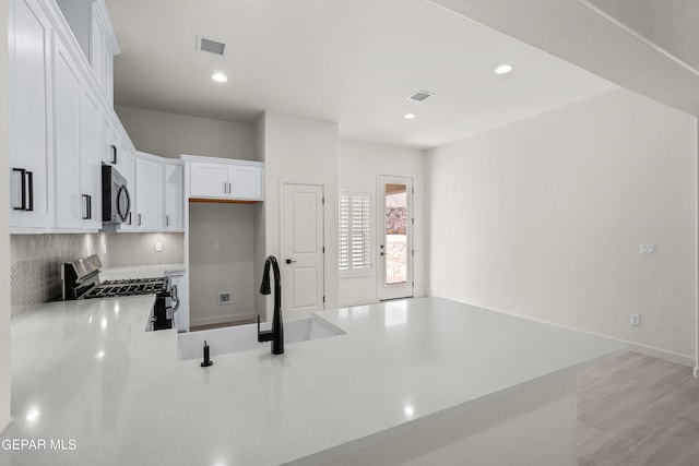 kitchen featuring white cabinetry, light hardwood / wood-style flooring, gas range, decorative backsplash, and sink