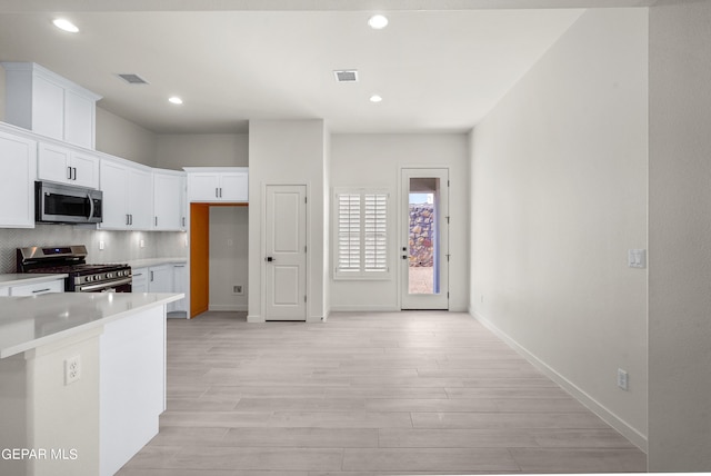 kitchen with appliances with stainless steel finishes, light hardwood / wood-style flooring, white cabinets, and backsplash