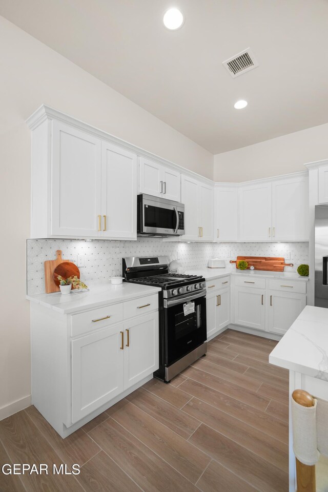 kitchen with decorative backsplash, light stone countertops, stainless steel appliances, light hardwood / wood-style flooring, and white cabinets