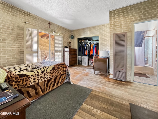 bedroom with a textured ceiling, light hardwood / wood-style flooring, brick wall, and a closet