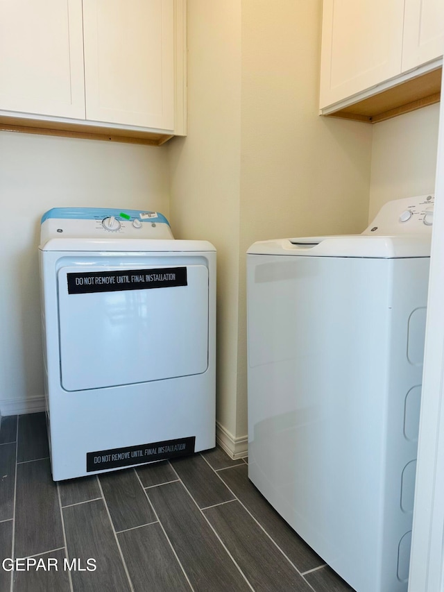 clothes washing area with washing machine and dryer, cabinets, and dark wood-type flooring