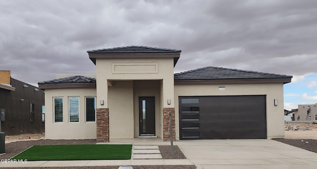 prairie-style house with a garage, concrete driveway, a tile roof, and stucco siding