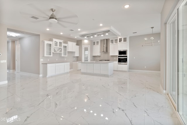 kitchen featuring recessed lighting, wall chimney exhaust hood, stainless steel microwave, marble finish floor, and ceiling fan with notable chandelier