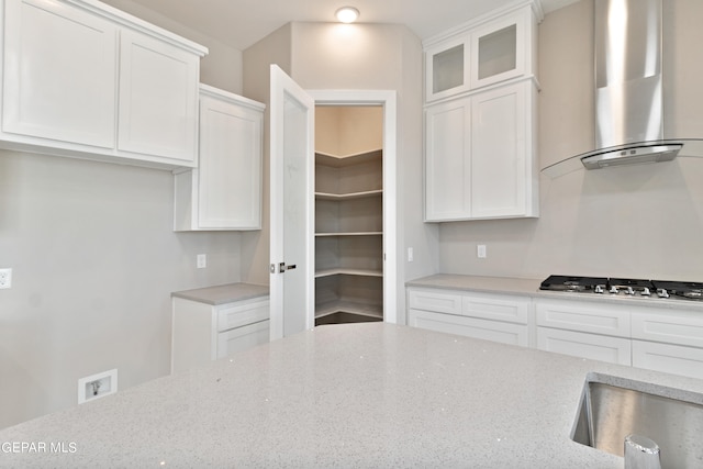 kitchen with stainless steel gas cooktop, wall chimney exhaust hood, light stone counters, and white cabinetry