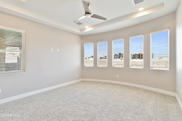 empty room with baseboards, visible vents, a raised ceiling, light colored carpet, and a healthy amount of sunlight