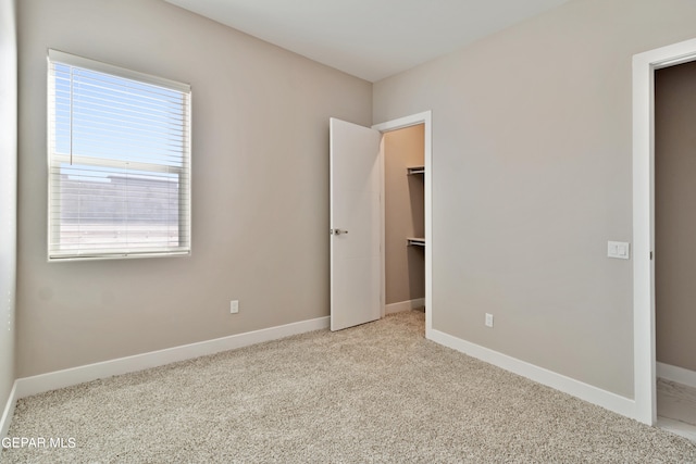 unfurnished bedroom with carpet floors, a closet, a spacious closet, and baseboards