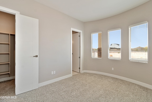 unfurnished bedroom featuring carpet floors, a walk in closet, and baseboards