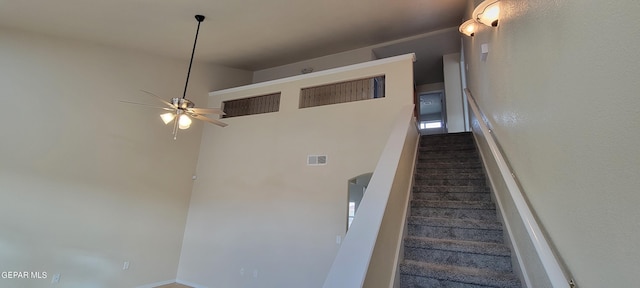 stairway with ceiling fan, carpet, and a towering ceiling