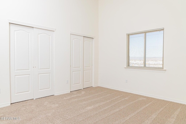 unfurnished bedroom with a towering ceiling, two closets, and light carpet