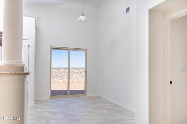 hallway with a towering ceiling, decorative columns, and light tile flooring