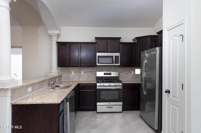 kitchen featuring appliances with stainless steel finishes, light stone countertops, decorative columns, and kitchen peninsula