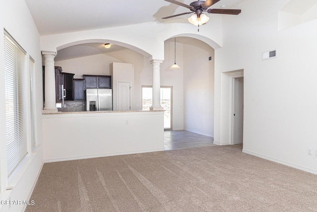 unfurnished living room with vaulted ceiling, light carpet, ceiling fan, and decorative columns