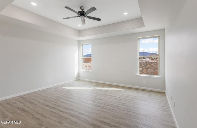 spare room with ceiling fan, light hardwood / wood-style flooring, and a tray ceiling