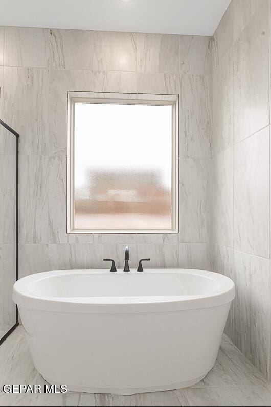 bathroom with a washtub, tile walls, and plenty of natural light