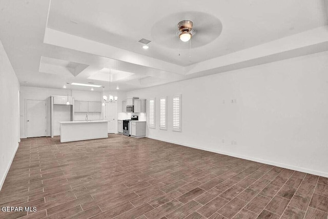 unfurnished living room with a tray ceiling, dark hardwood / wood-style floors, and ceiling fan with notable chandelier