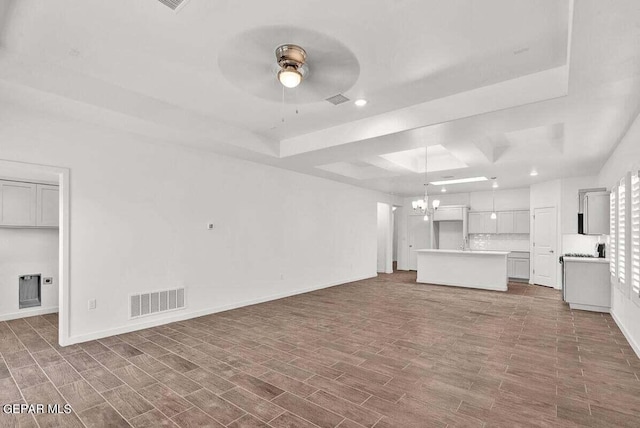 unfurnished living room featuring a raised ceiling, sink, and ceiling fan with notable chandelier