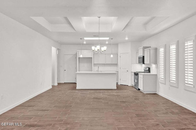 kitchen with decorative light fixtures, coffered ceiling, appliances with stainless steel finishes, a kitchen island with sink, and backsplash