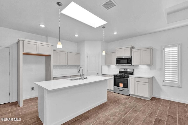 kitchen with appliances with stainless steel finishes, hanging light fixtures, tasteful backsplash, sink, and a center island with sink