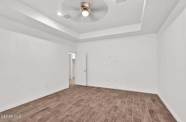 empty room featuring a raised ceiling, ceiling fan, and dark hardwood / wood-style floors