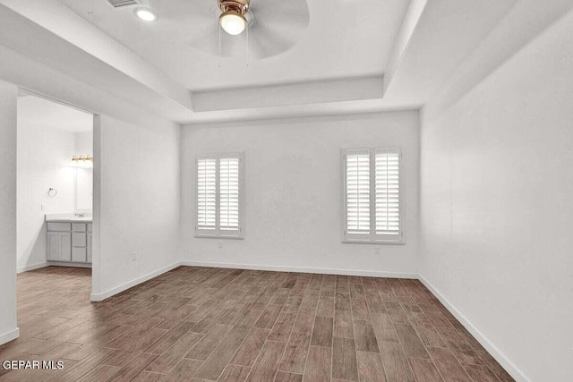 unfurnished room featuring a tray ceiling, a healthy amount of sunlight, ceiling fan, and dark wood-type flooring