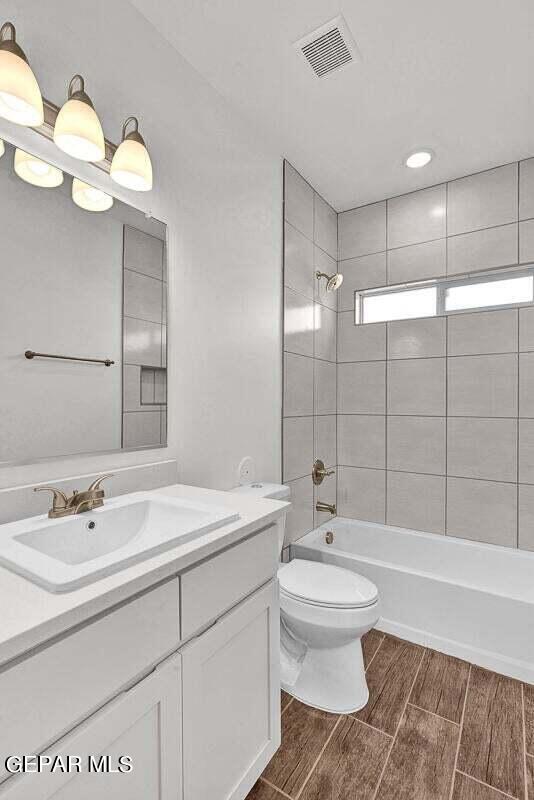 full bathroom featuring hardwood / wood-style floors, toilet, tiled shower / bath combo, and vanity