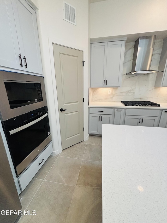 kitchen featuring light countertops, visible vents, tasteful backsplash, appliances with stainless steel finishes, and wall chimney range hood
