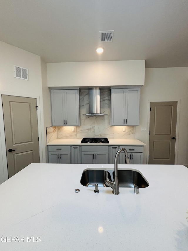 kitchen with tasteful backsplash, gray cabinetry, a sink, visible vents, and wall chimney range hood