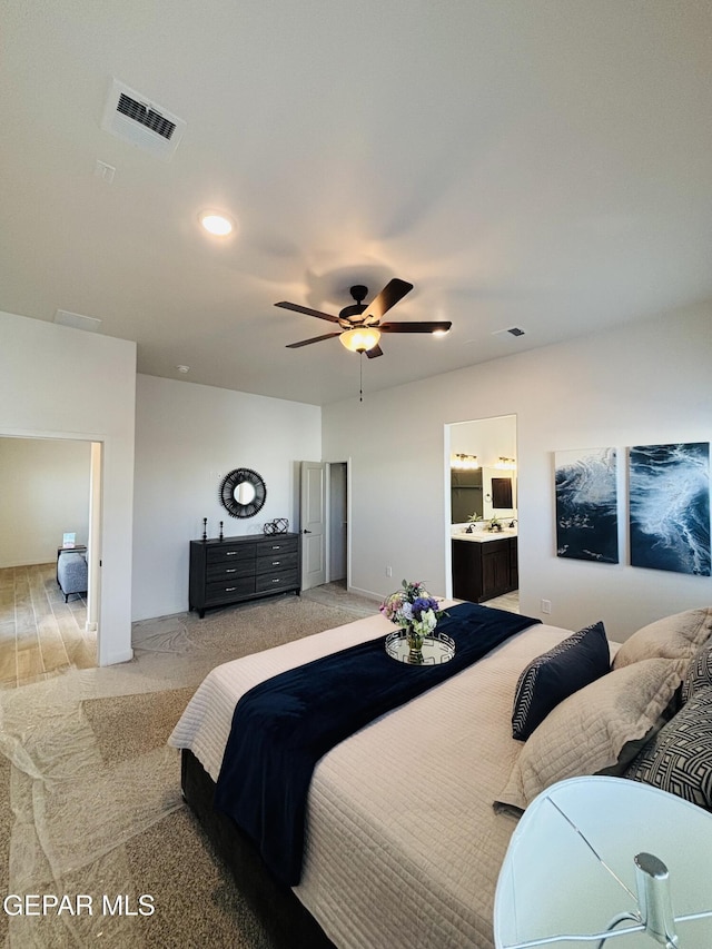bedroom with light colored carpet, visible vents, ensuite bath, and a ceiling fan