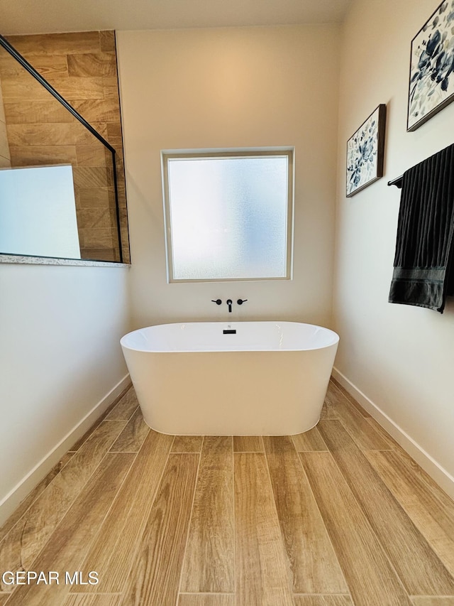 full bathroom featuring baseboards, wood finished floors, a tile shower, and a freestanding bath
