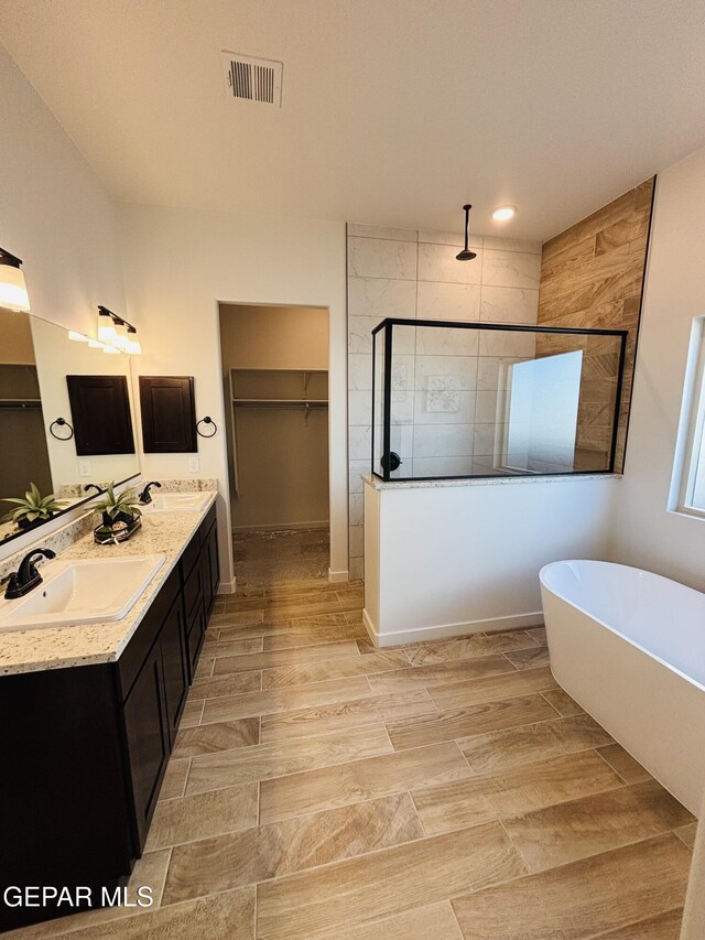 bathroom with a sink, a walk in closet, a soaking tub, walk in shower, and visible vents