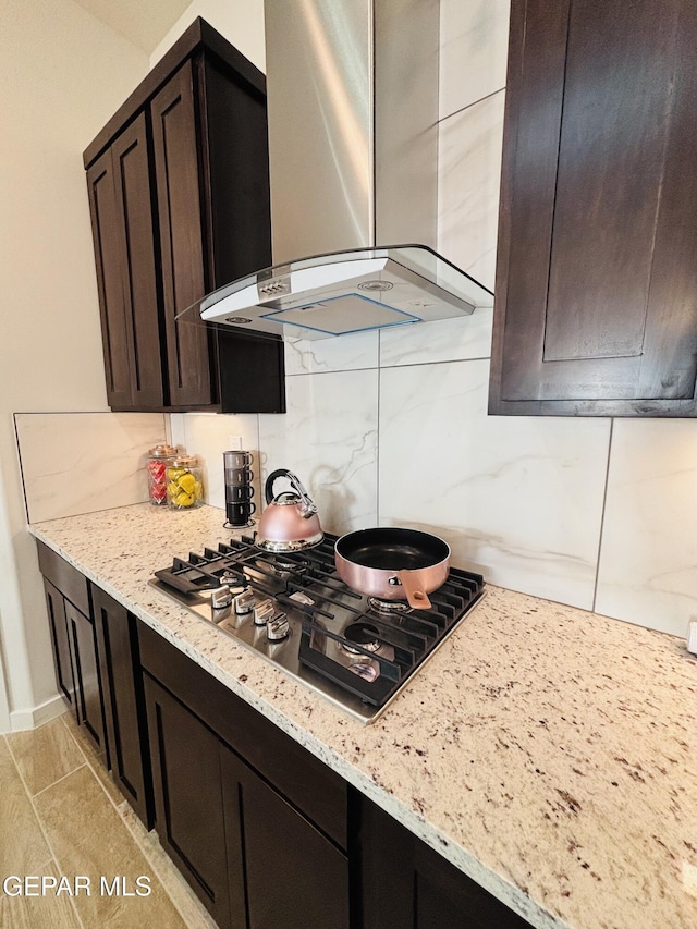 kitchen with wall chimney range hood, stainless steel gas cooktop, light stone countertops, and tasteful backsplash