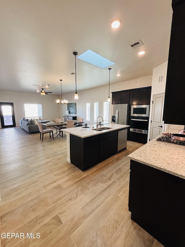 kitchen featuring light stone counters, a sink, dark cabinetry, open floor plan, and stainless steel appliances