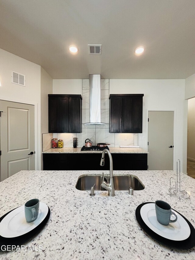 kitchen featuring a sink, visible vents, wall chimney range hood, and light stone counters