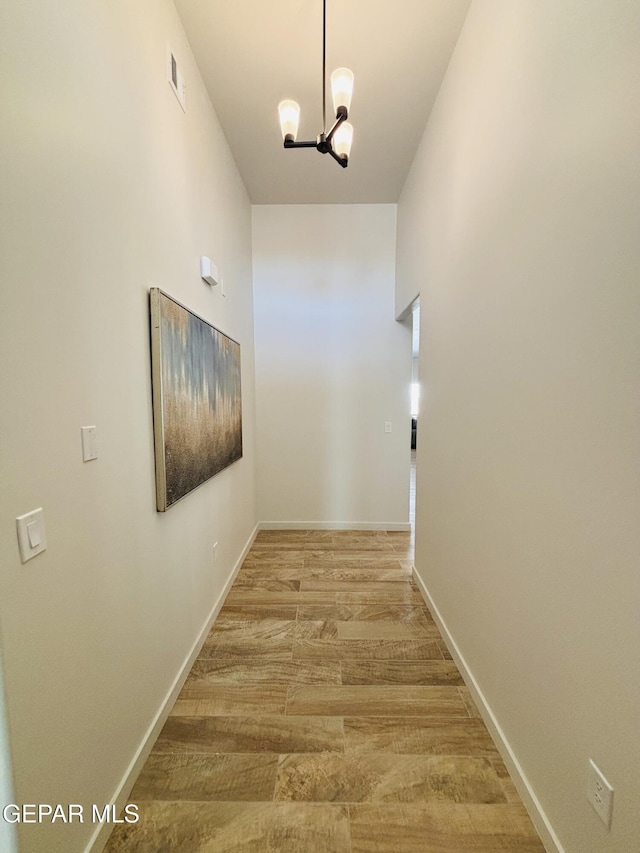 corridor featuring baseboards, visible vents, a chandelier, and light wood-style floors