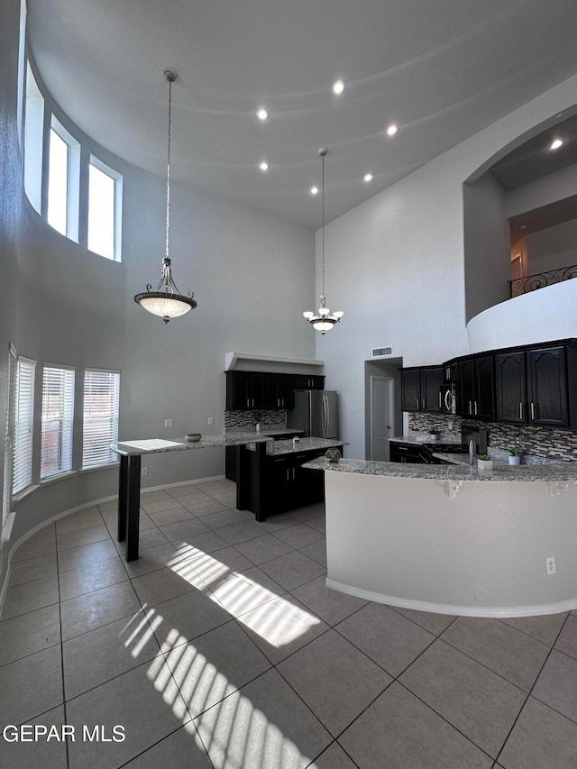 kitchen with stainless steel fridge, hanging light fixtures, light tile floors, and a high ceiling