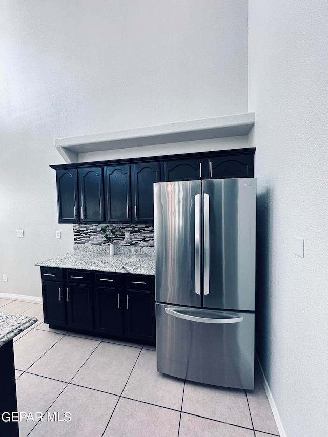 kitchen with light stone countertops, tasteful backsplash, stainless steel refrigerator, and light tile flooring