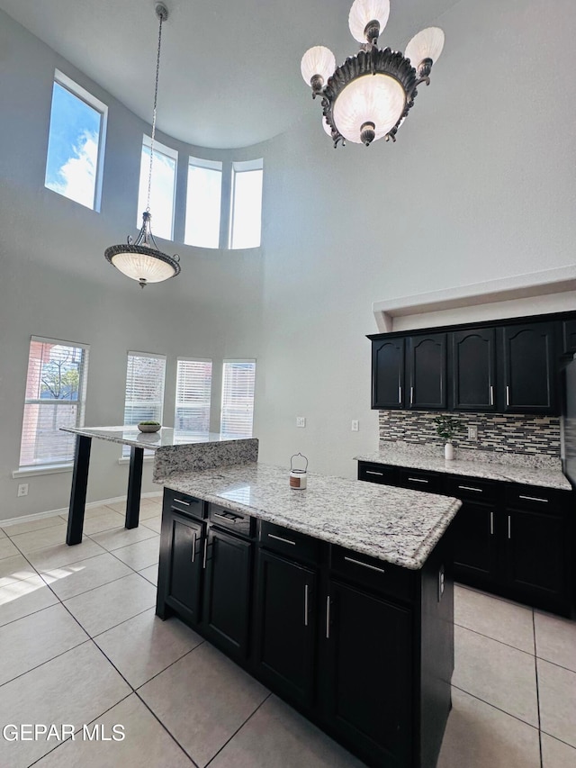 kitchen featuring decorative light fixtures, light tile flooring, light stone countertops, a high ceiling, and tasteful backsplash