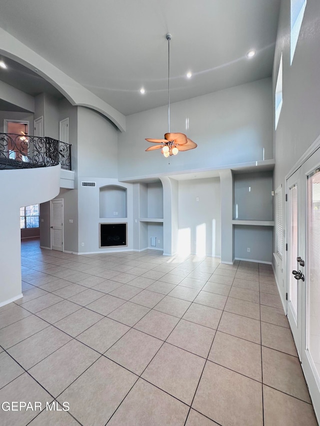 unfurnished living room with a towering ceiling, ceiling fan, light tile flooring, and built in shelves